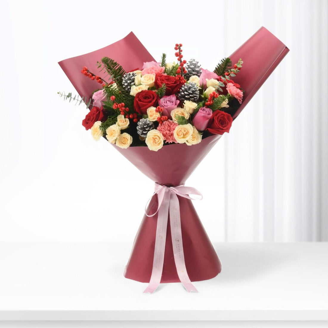 Vibrant red, pink, and cream roses nestled with pinecones and berries in burgundy wrap.