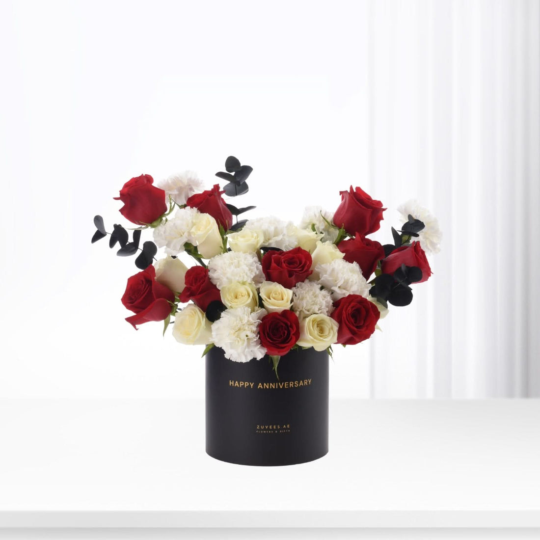 Elegant black box holds vibrant red, white roses and black eucalyptus for anniversary.