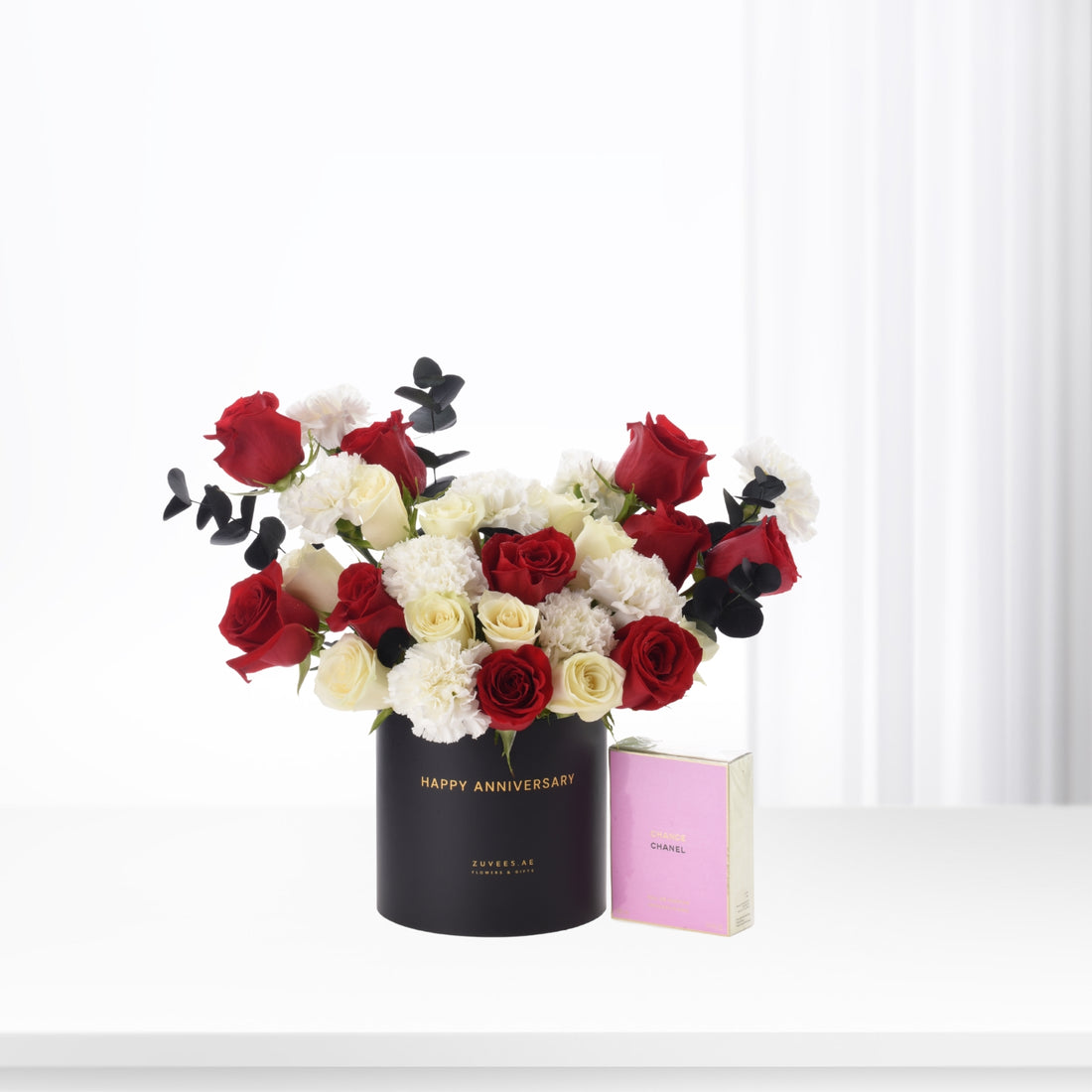 Elegant black vase with red, white roses and eucalyptus, beside pink Chanel perfume.