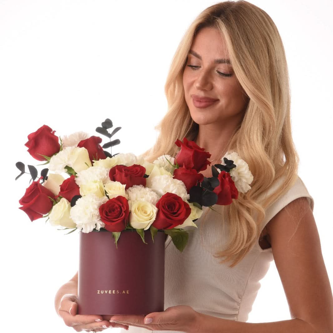 Woman holds burgundy box of red and white roses with black eucalyptus.