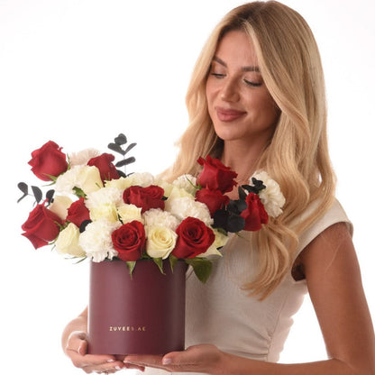 Woman holds burgundy box of red and white roses with black eucalyptus.