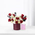 Luxurious red, white, and black rose bouquet in burgundy cylinder beside pink Chanel perfume.