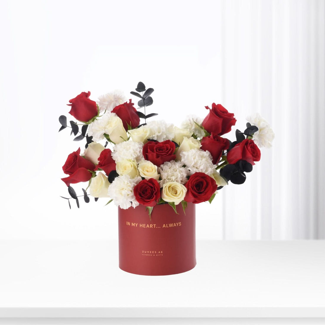 Vibrant red, white roses and carnations in elegant red box with golden "In My Heart... Always" inscription.