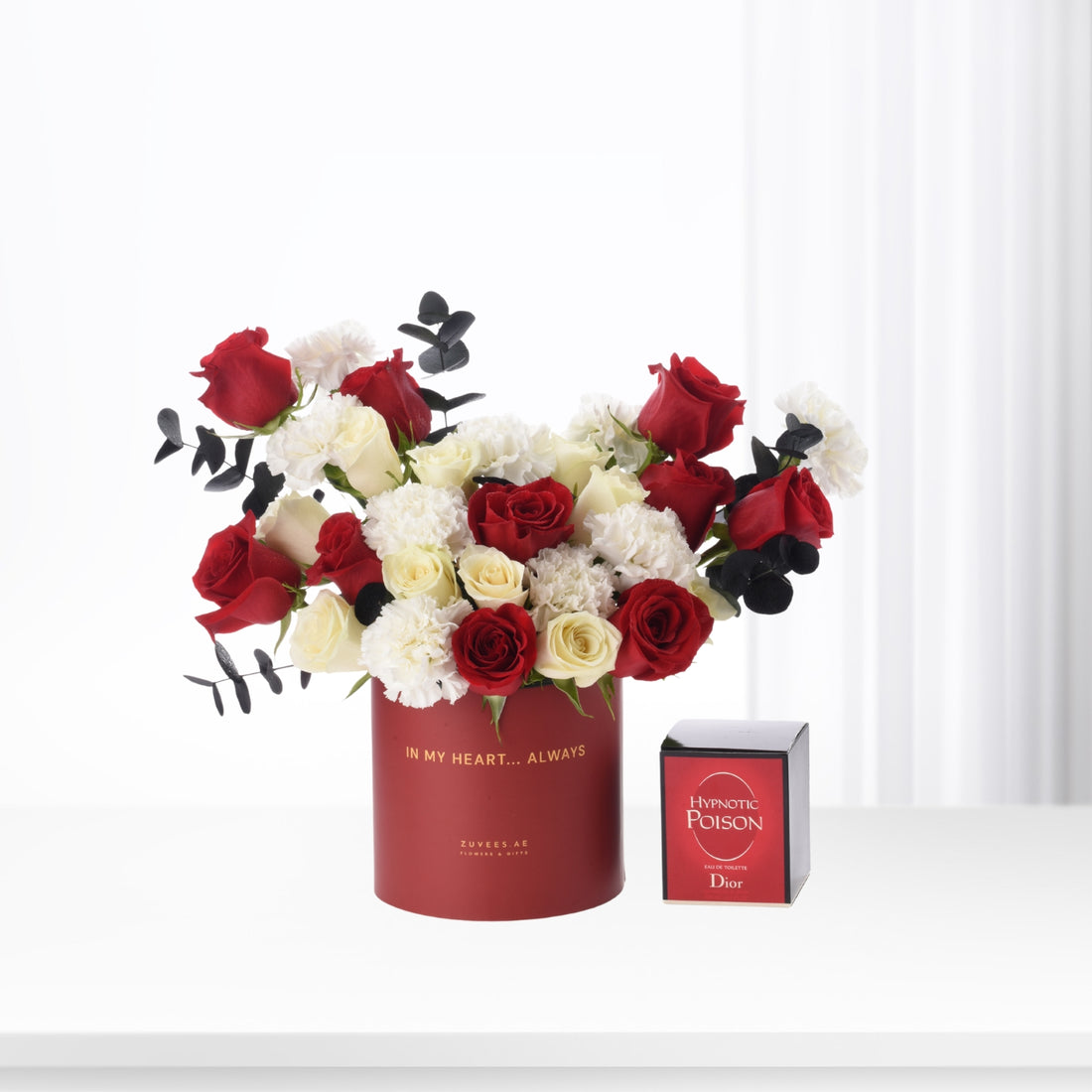 Bold red, white, and black floral arrangement in branded red cylinder beside Dior Hypnotic Poison perfume.