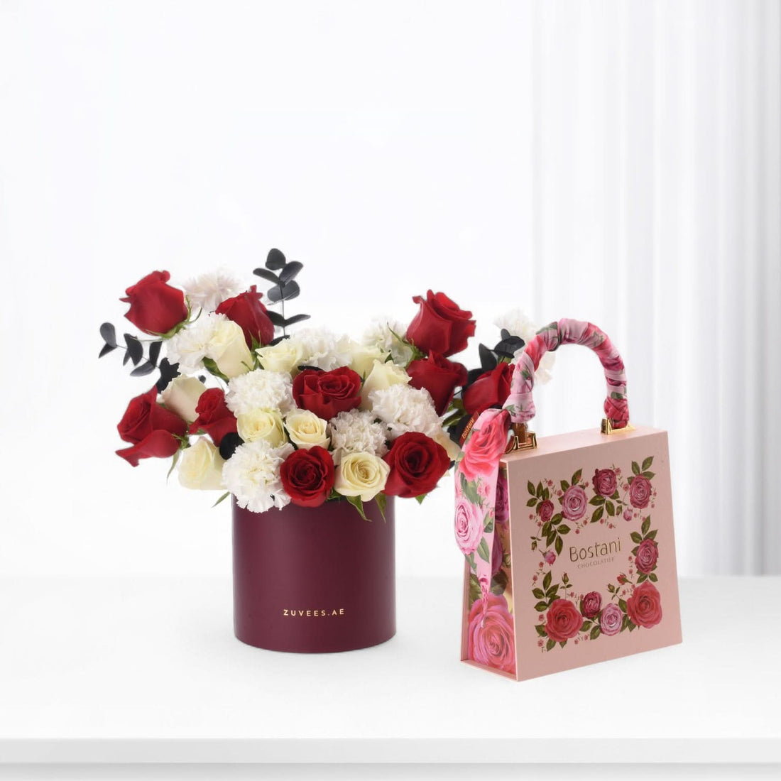 Luxurious red, white rose bouquet with carnations and eucalyptus, paired with elegant pink Bostani chocolate gift bag.