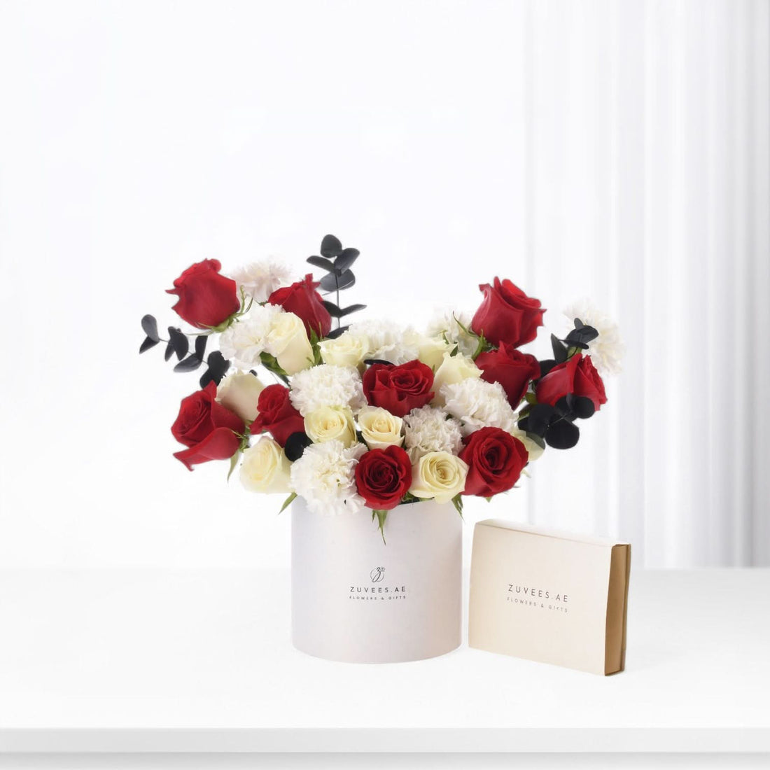 Elegant red, white roses and carnations in minimalist white cylindrical vase with branded packaging.
