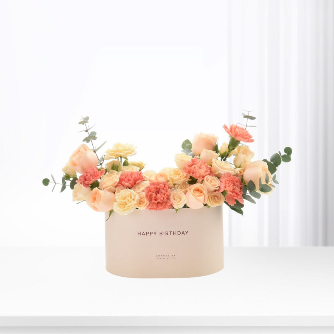 Pastel peach roses and carnations in cream box with "Happy Birthday" text.