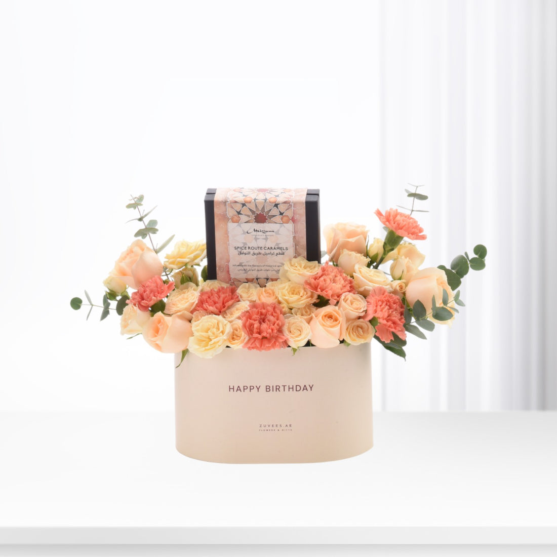 Pastel peach roses and carnations surround a spice caramel gift in a "Happy Birthday" box.