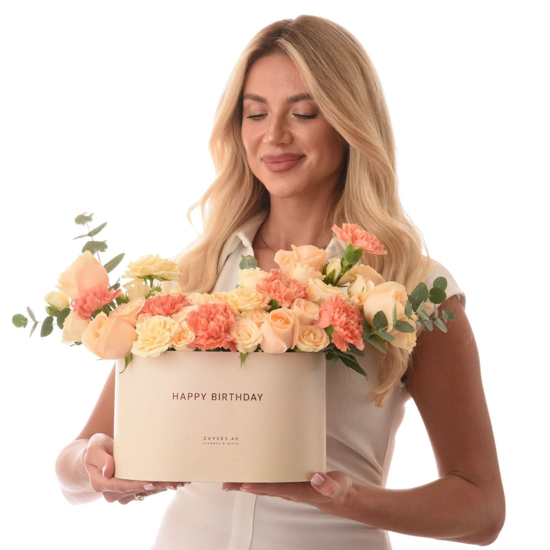 Blonde woman holds creamy box overflowing with peach roses and carnations.