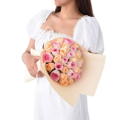 Soft pink and peach roses wrapped in cream paper, held by a woman in white.