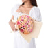 Soft pink and peach roses wrapped in cream paper, held by a woman in white.