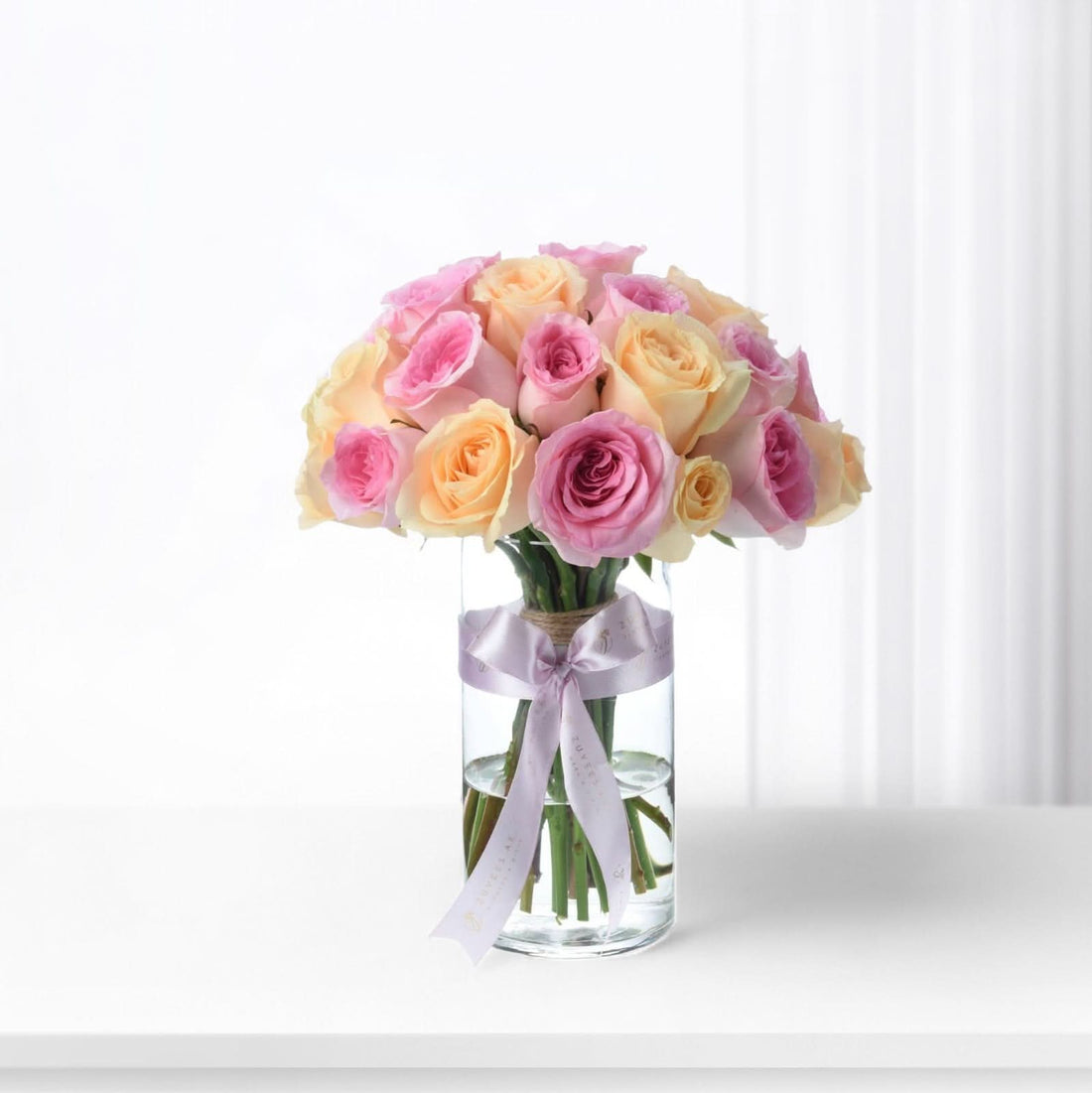 Pastel pink and peach roses in clear glass vase with lavender ribbon.