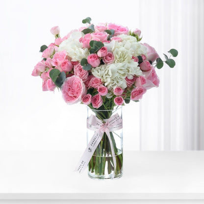 Pink roses and white hydrangeas in clear vase with branded ribbon.