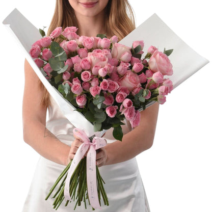 Soft pink roses wrapped in white paper, tied with branded ribbon.