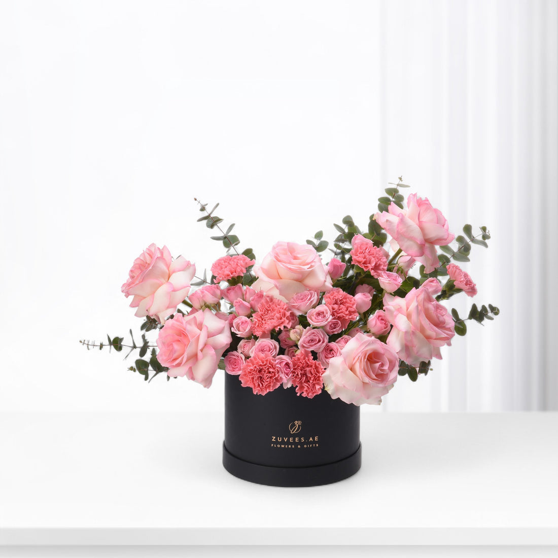 Elegant pink roses and carnations in sleek black box with gold logo.