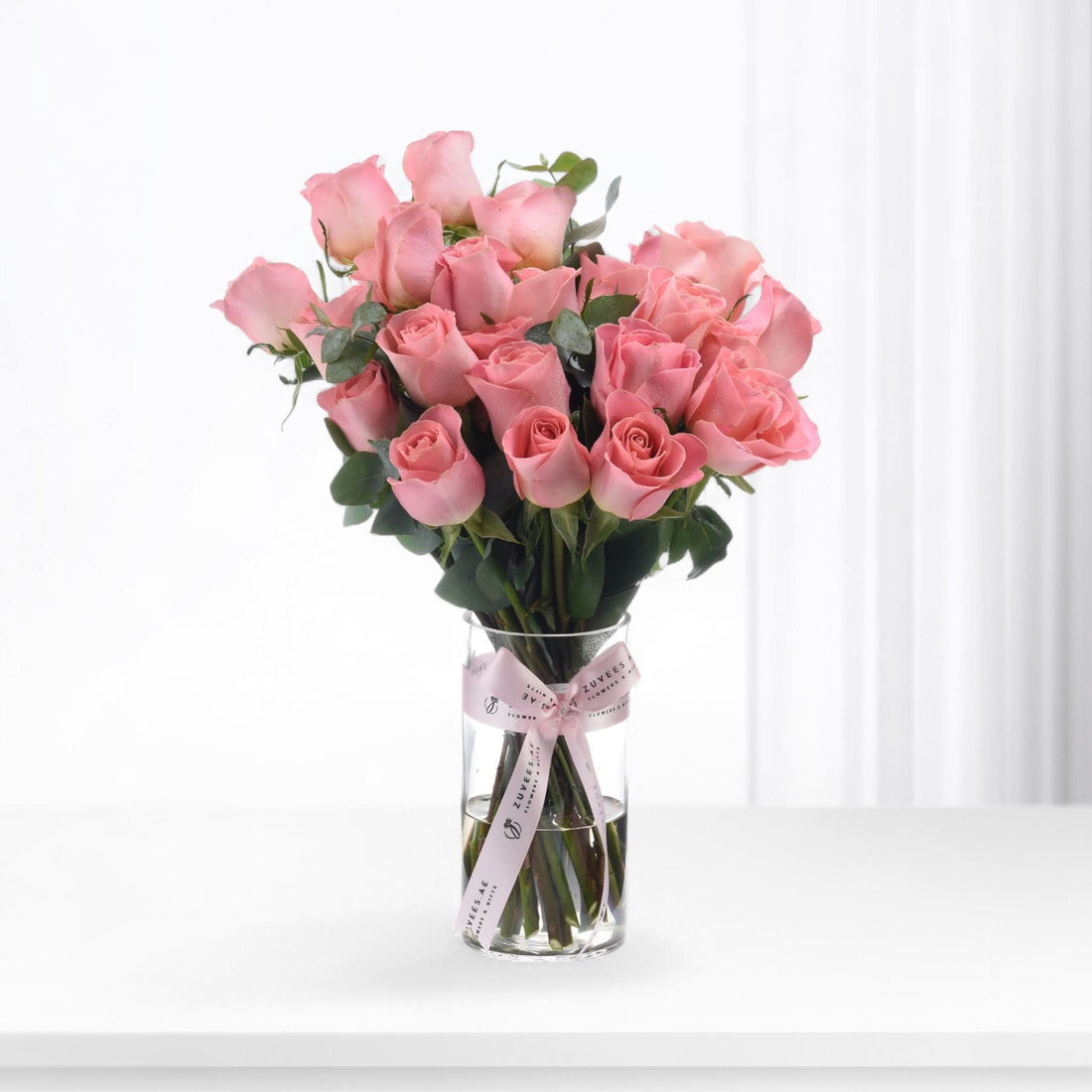 Soft pink roses in clear vase, tied with branded pink ribbon.