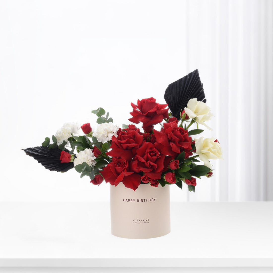 Bold red roses, white blooms, and black fan leaves in "Happy Birthday" vase.