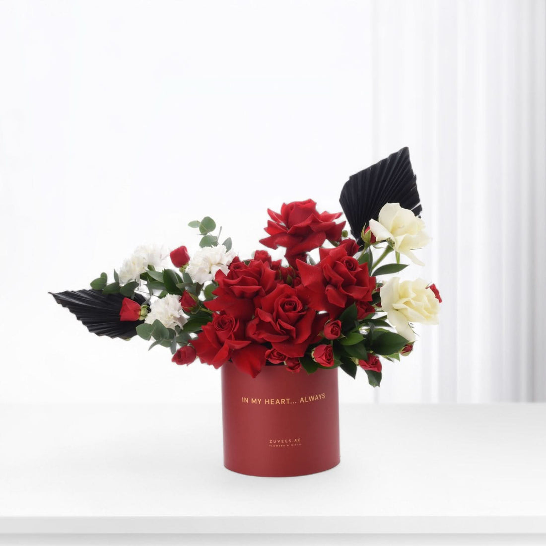 Vibrant red and white roses in sleek red box with gold text.