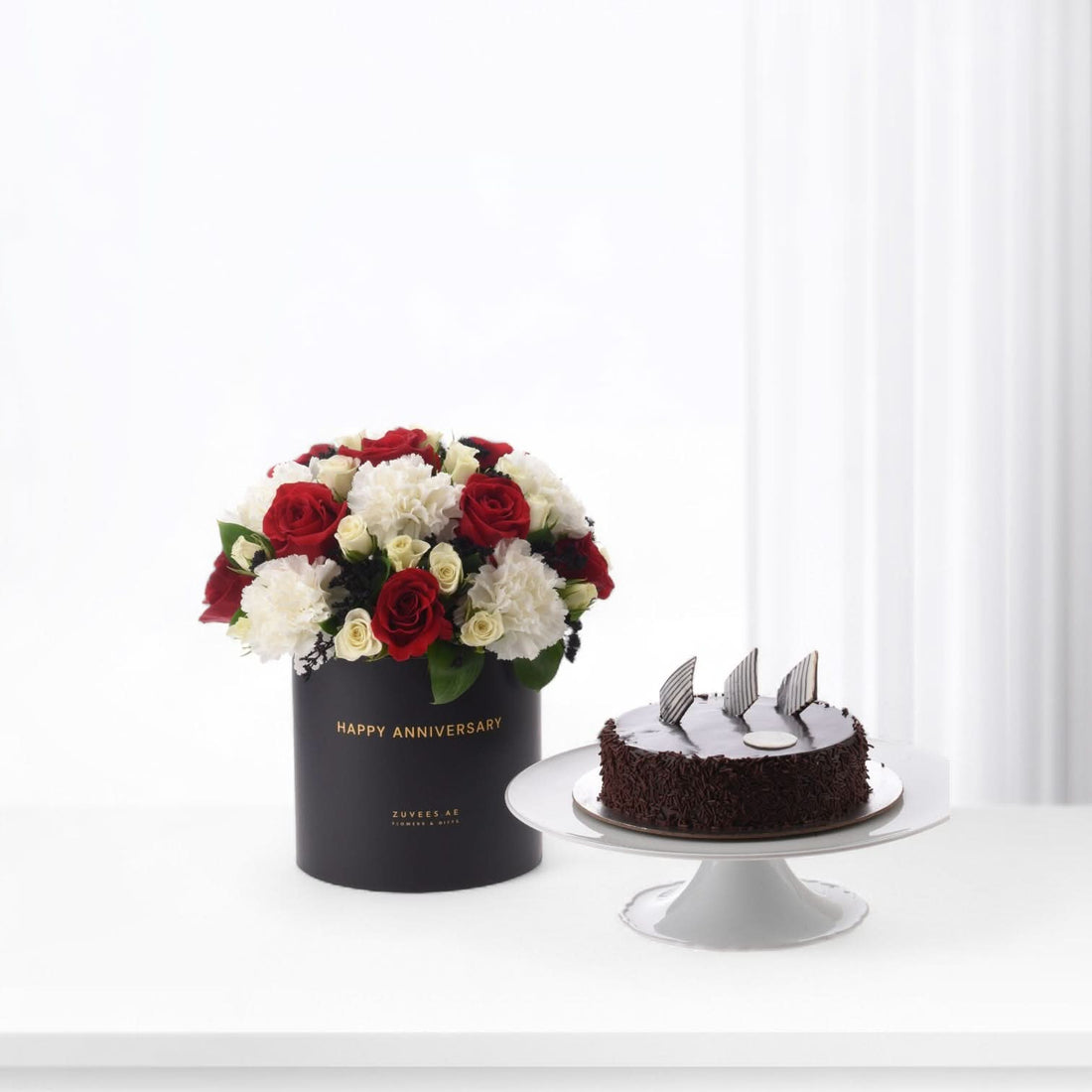 Elegant red and white roses in black box beside chocolate cake.