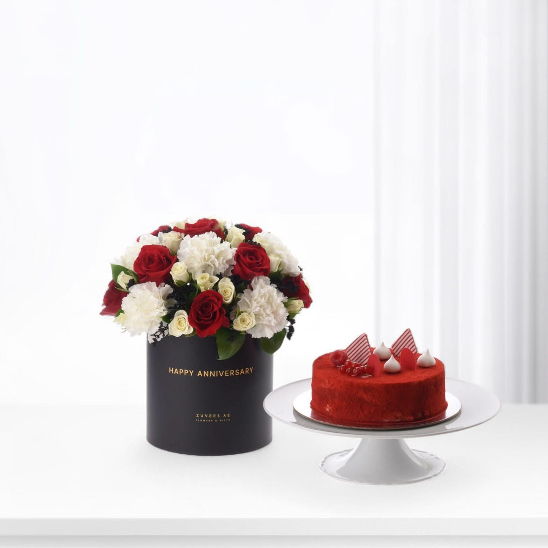 Elegant red and white roses in black box beside vibrant red velvet cake.