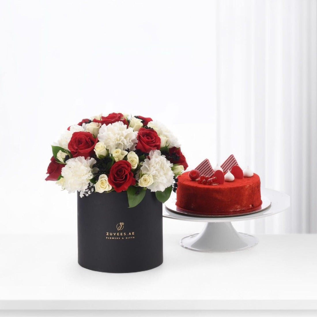 Elegant red and white roses in black box beside vibrant red velvet cake.