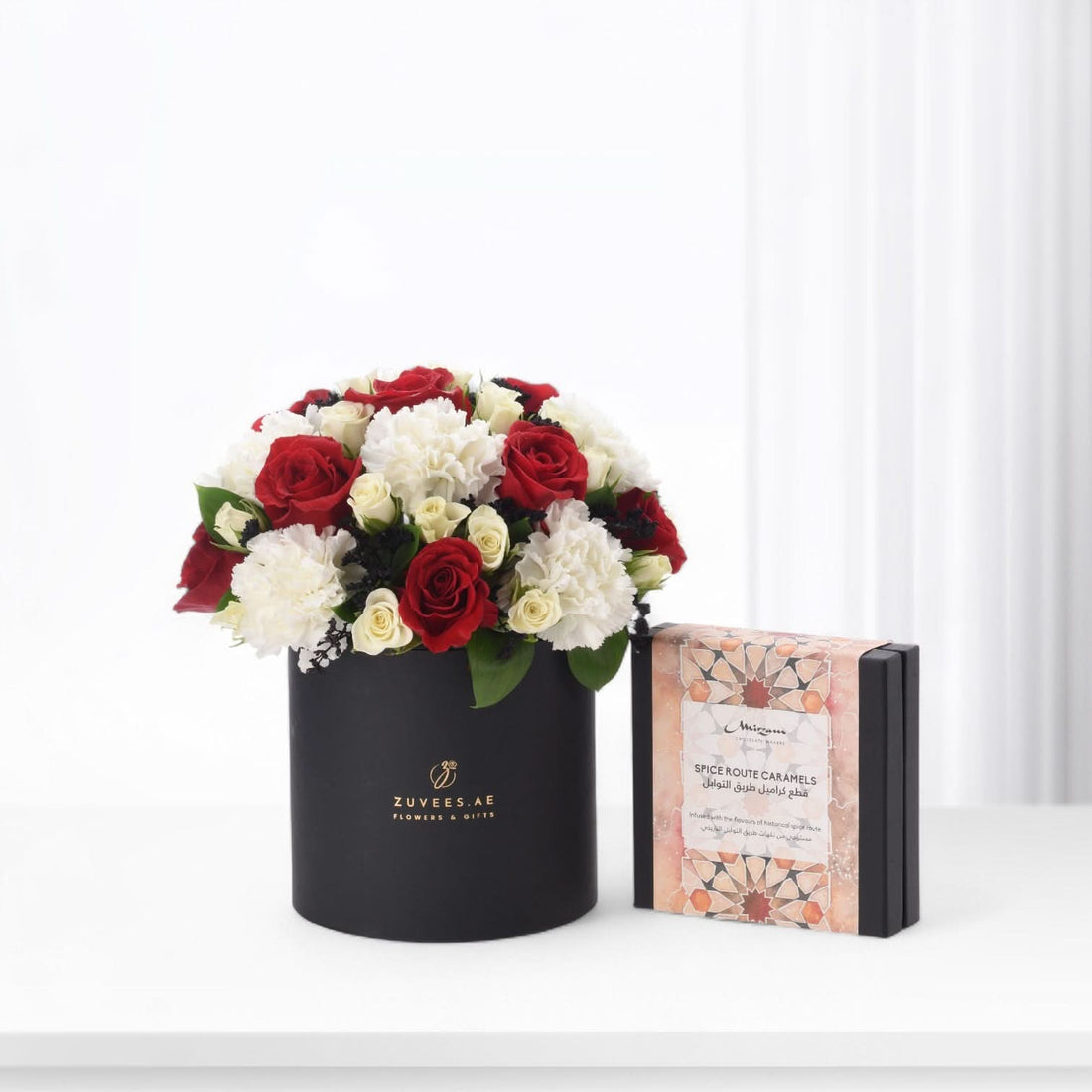 Elegant black box holds vibrant red roses and white carnations, paired with ornate caramel gift box.