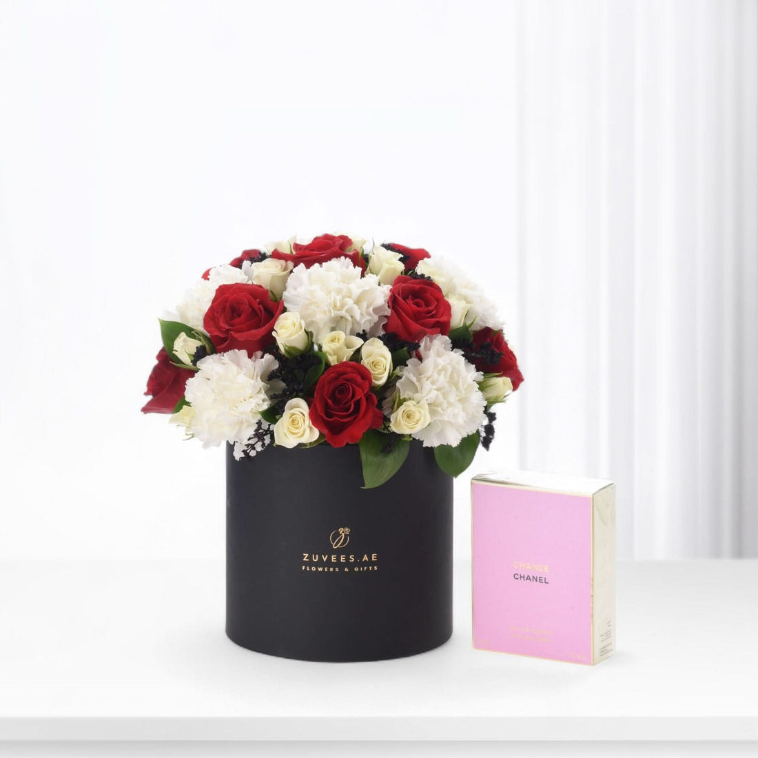 Elegant black hat box with red and white roses, beside pink Chanel perfume.