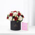 Elegant black hat box with red and white roses, beside pink Chanel perfume.