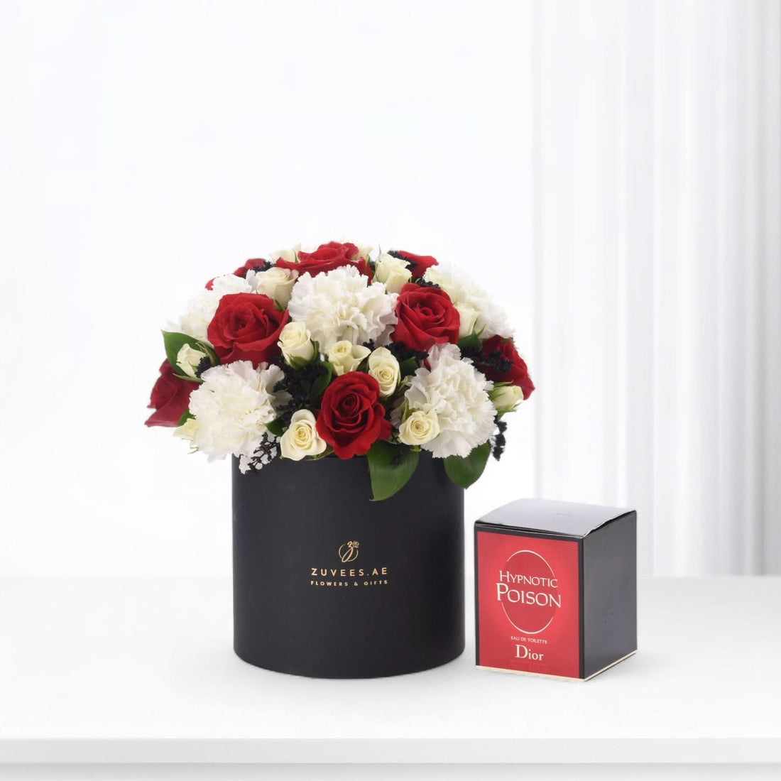 Elegant red and white roses in black box beside Dior Hypnotic Poison perfume.