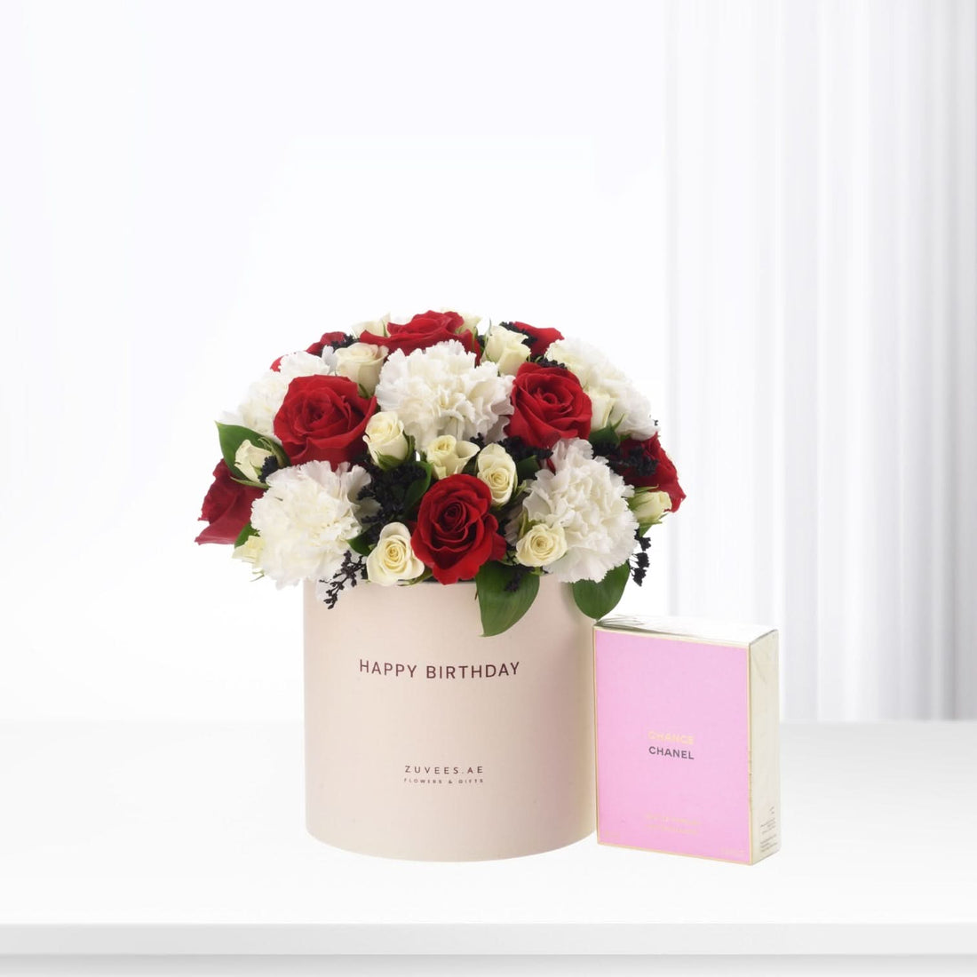 Elegant red and white roses in blush box beside pink Chanel perfume.