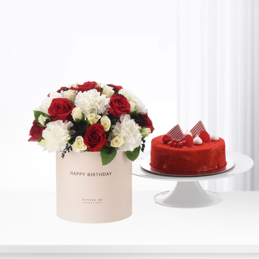 Red and white roses in beige box beside red velvet cake.