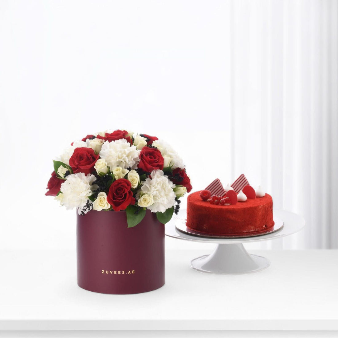 Red velvet cake beside burgundy floral box with red and white roses, elegant gift set.
