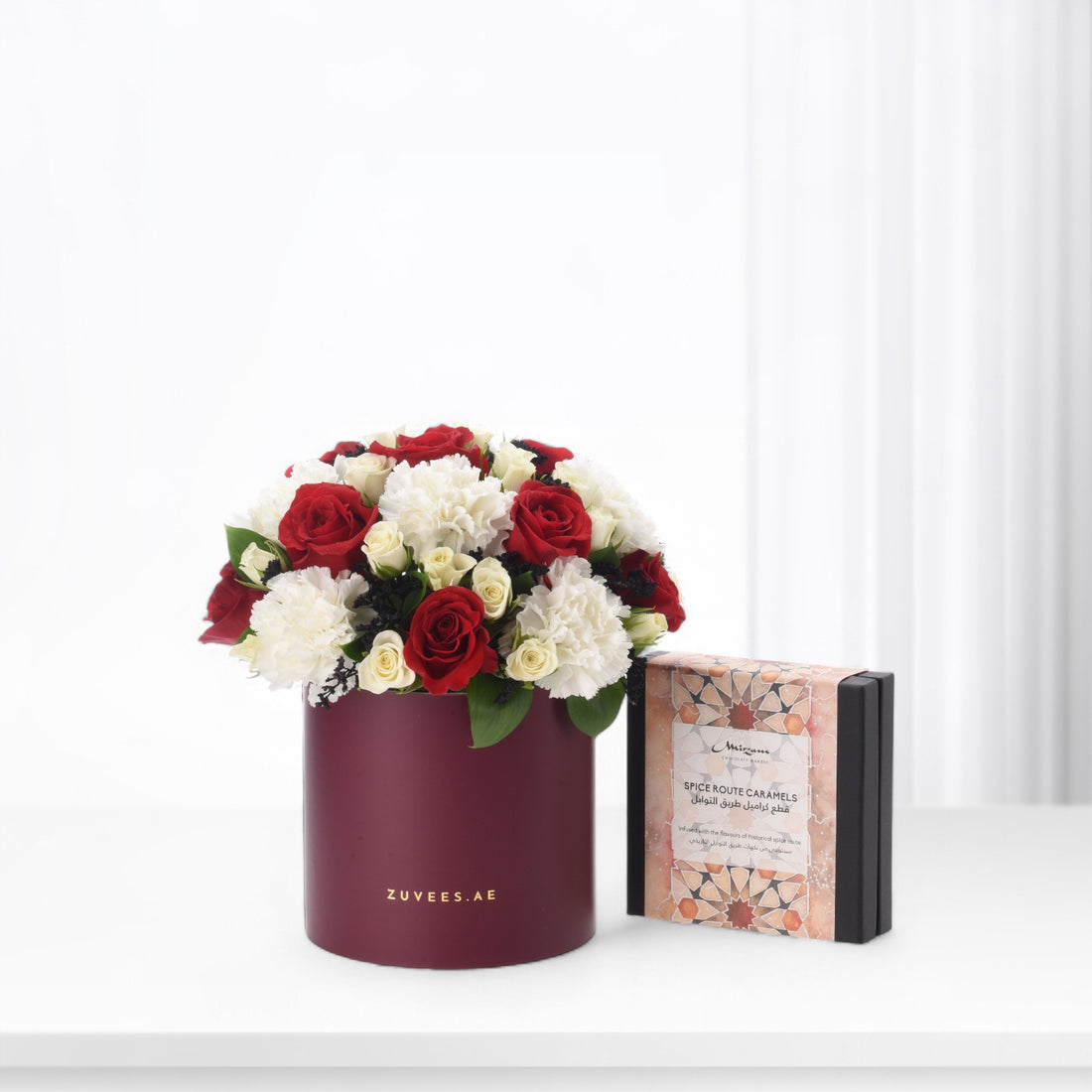 Elegant red and white roses in burgundy box beside ornate caramel gift box.