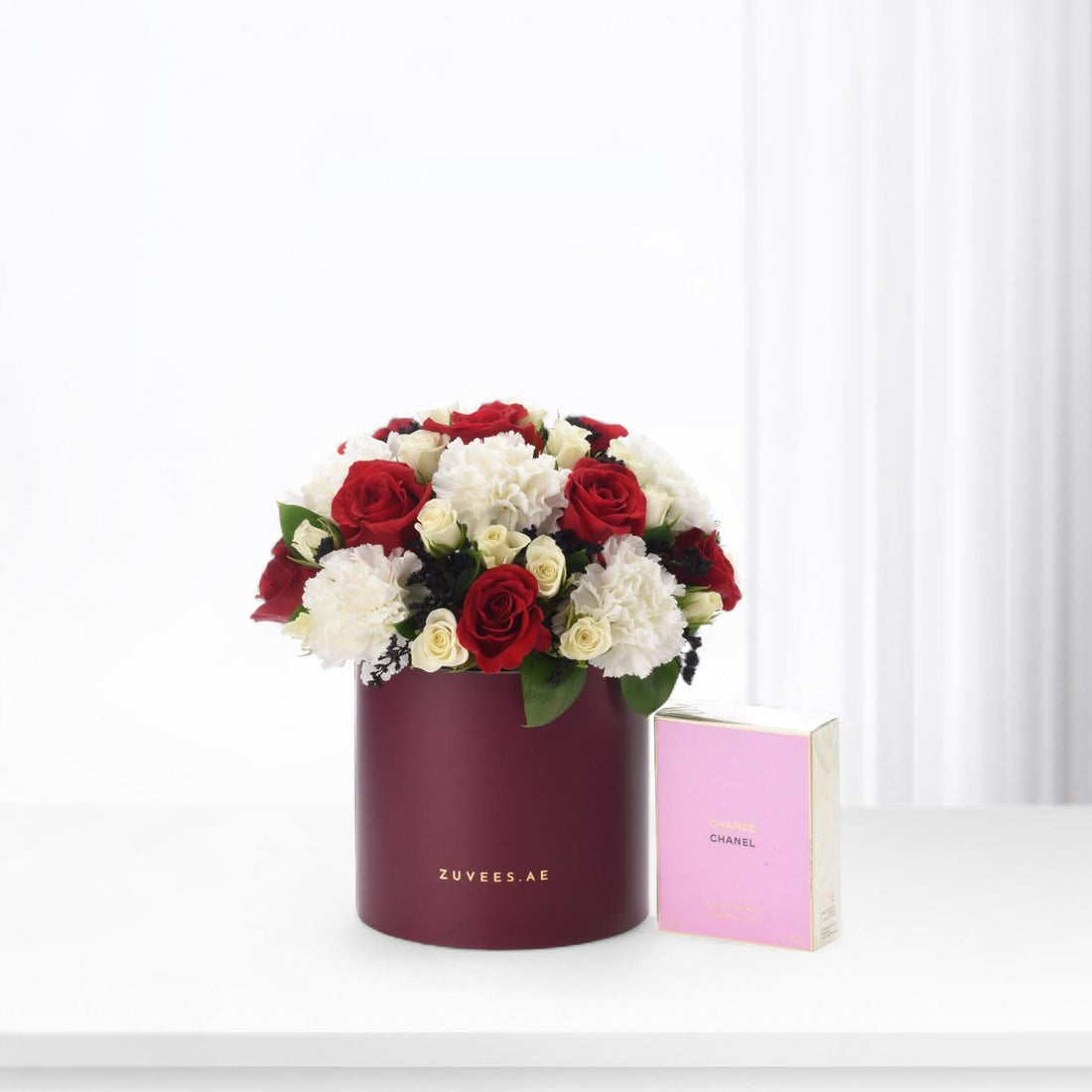Elegant red and white roses in burgundy box beside pink Chanel perfume.