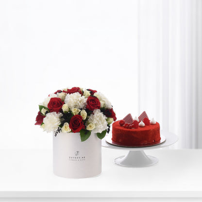 Red roses and white carnations in white box beside red velvet cake.