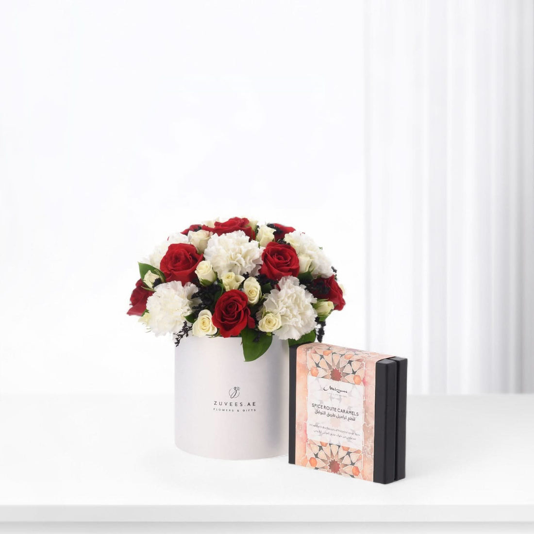 Elegant red and white roses in white box beside ornate caramel gift box.