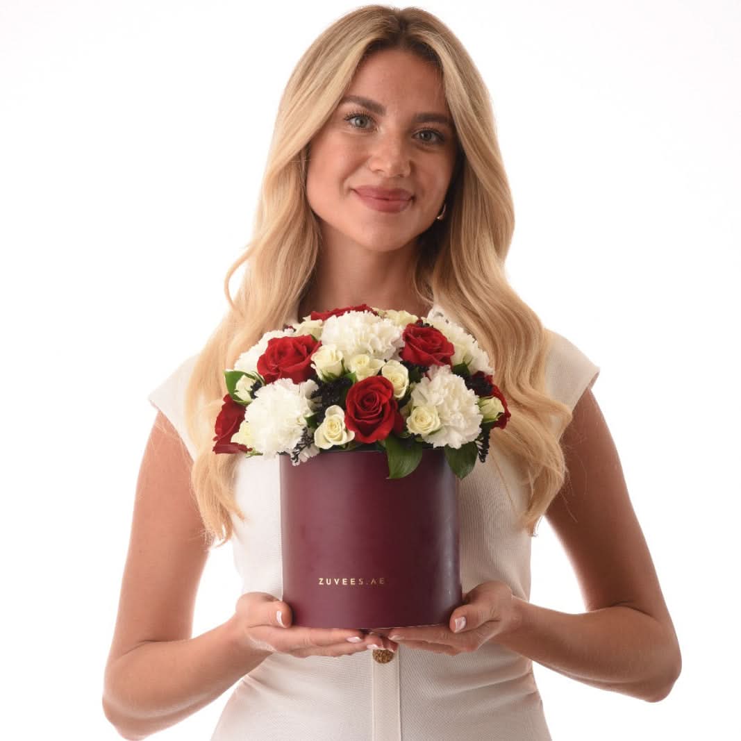 Woman holds burgundy box of red and white roses, elegant and vibrant.