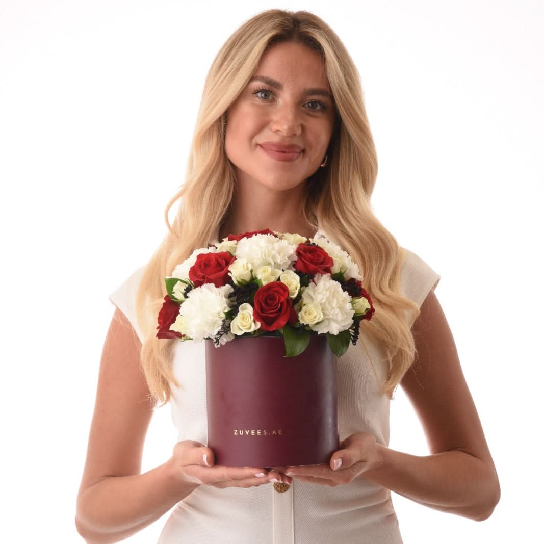 Woman holds burgundy box with red and white roses against white background.