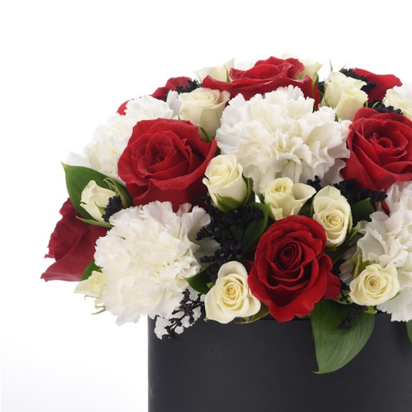 Bold red roses, creamy white carnations, and dark accents in sleek black vase.