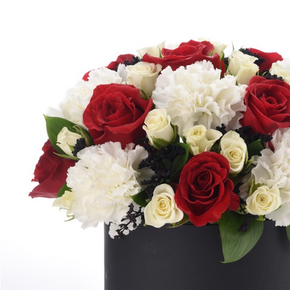 Bold red roses, creamy white carnations, and dark accents in sleek black vase.