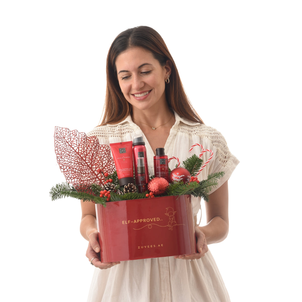 Shimmering red holiday gift box with festive greenery and branded skincare products.