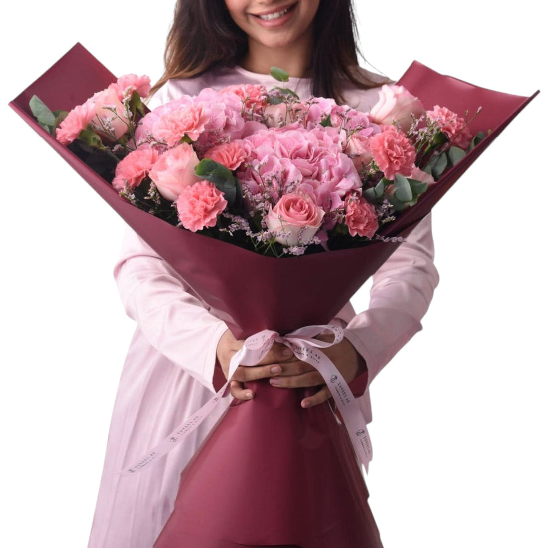 Pink roses, carnations, and hydrangeas wrapped in burgundy paper with ribbon.