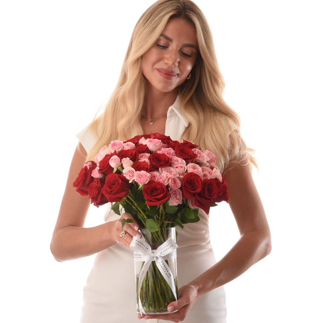 Woman holds vibrant red and pink roses in clear vase with white ribbon.
