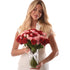 Woman holds vibrant red and pink roses in clear vase with white ribbon.