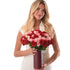 Woman holds lush red and pink roses in sleek burgundy vase.