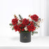 Vibrant red roses, pine, cotton, and a glittering ornament in a matte black cylinder.