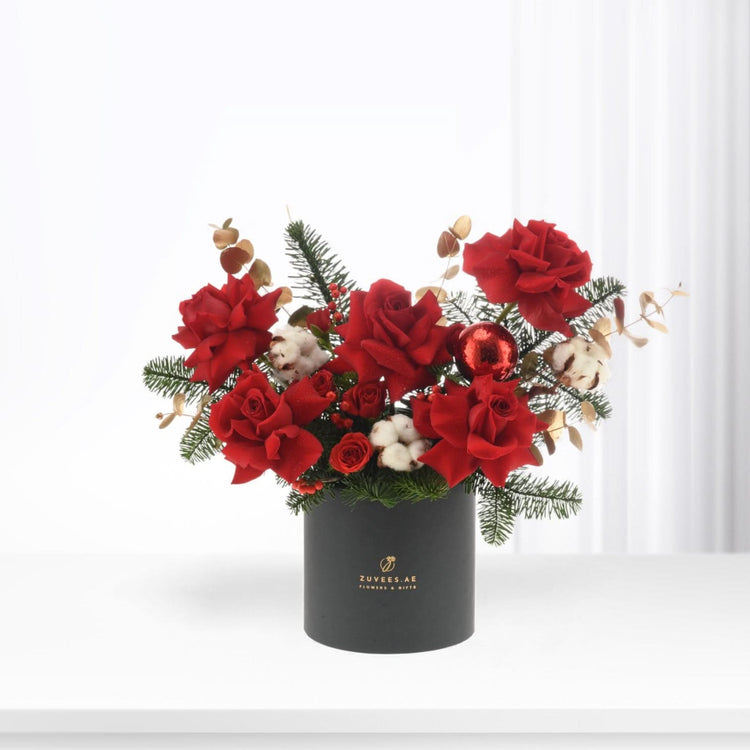 Vibrant red roses, pine, cotton, and a glittering ornament in a matte black cylinder.