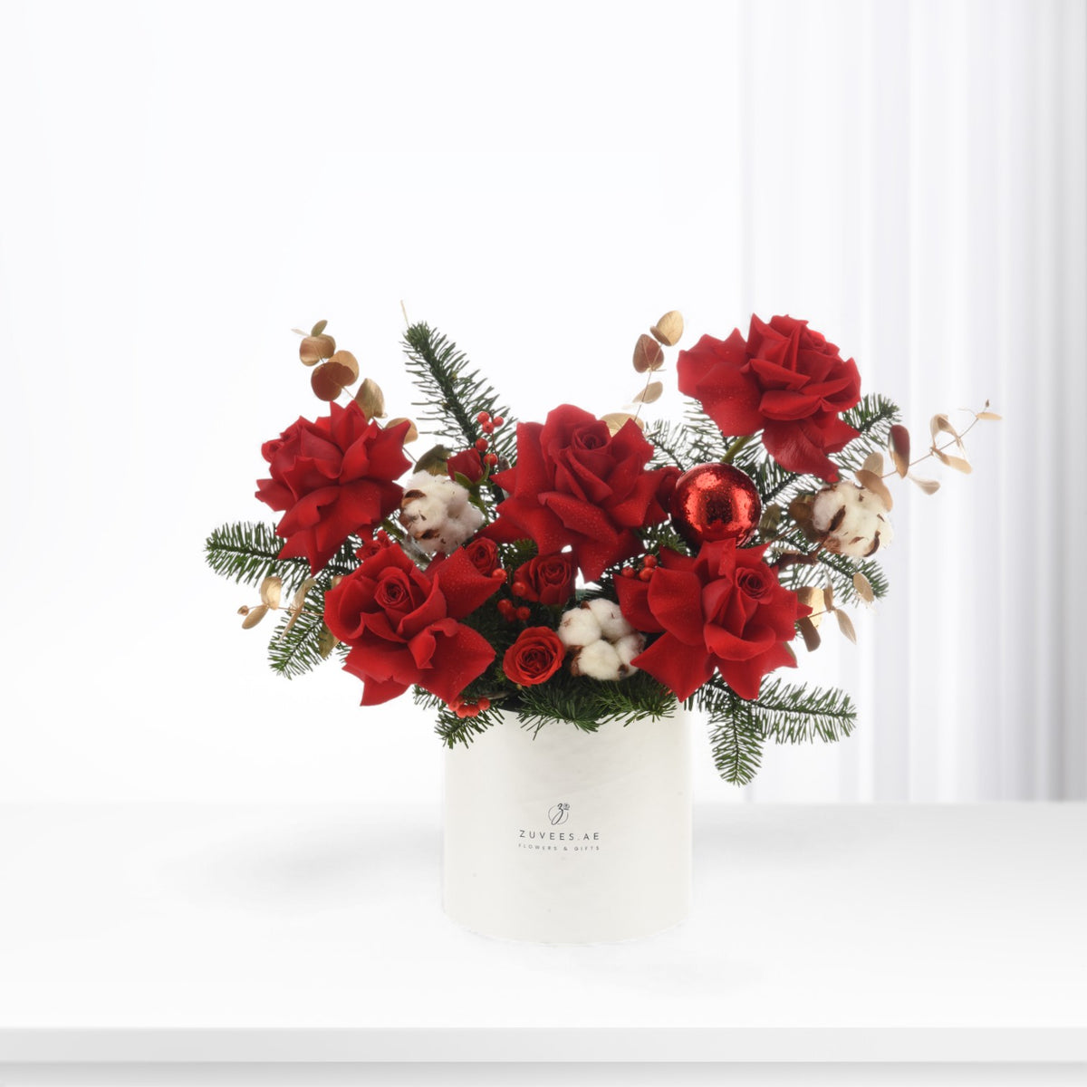 Vibrant red roses, pine, cotton, and berries in white vase.