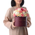 Woman holds burgundy "Happy Birthday" box filled with vibrant pink, peach, and white roses.