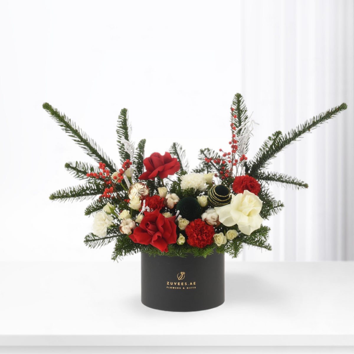 Elegant holiday floral arrangement in black box with red roses, white blooms, and evergreens.